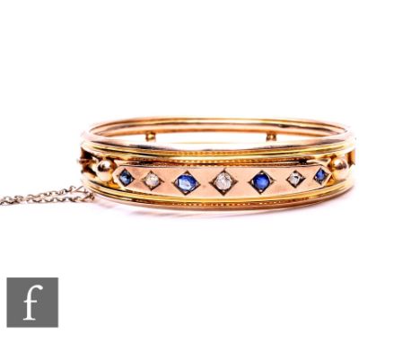 An early 20th Century 9ct hinged bangle set with seven alternating sapphires and diamonds to a raised central panel, weight 1