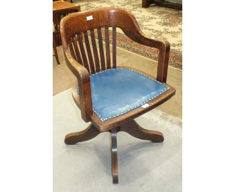 A 1920's/1930's oak revolving tilt-action office armchair with slatted back and shaped seat, on quadruped base.