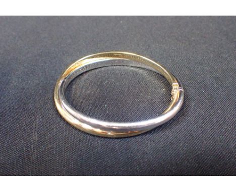 A 9CT BI-COLOURED GOLD HINGED BANGLE BY S&amp;C of twisted form, with double safety catch, stamped '375' to both colours, in 
