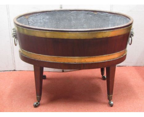 A Georgian mahogany wine cooler of oval form, brass banded with lion marks and ring handles, raised on square tapered legs wi