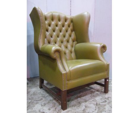 A reproduction Georgian style light green leather upholstered wing armchair with button back and studded detail raised on squ