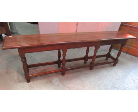 A low old English style walnut bench stool, the rectangular planked seat with moulded outline raised on eight turned supports