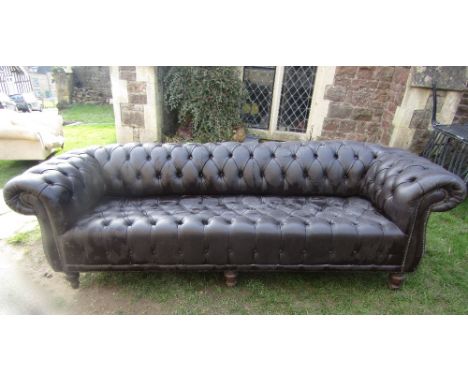 A substantial buttoned Chesterfield sofa in a dark brown colourway, raised on turned supports, 2.5m long approx.