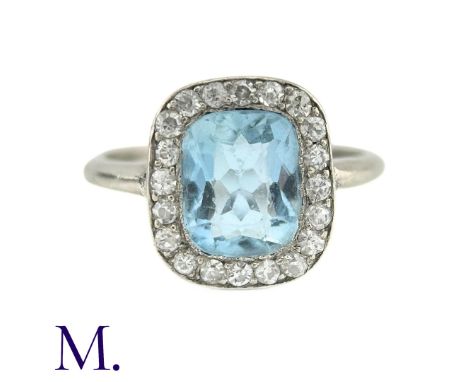 An Aquamarine And Diamond Cluster Ring in white gold, the principal cushion cut aquamarine surrounded by a border of round cu