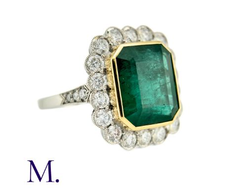 An Emerald And Diamond Cluster Ring in platinum, the central rectangular step cut emerald of 6.52cts surrounded by a border o