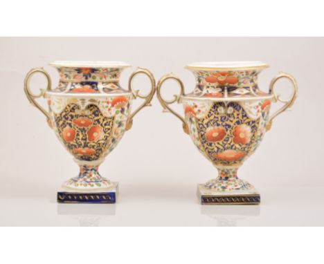 A pair of Derby porcelain campana shaped urns, early 19th Century, each with twin scrolled handles, decorated in underglaze b