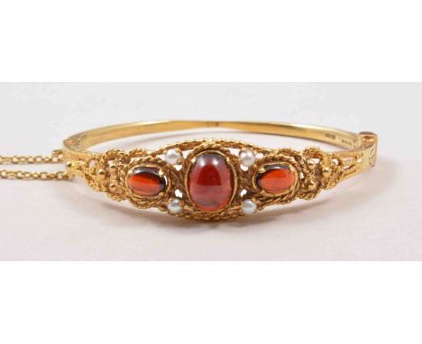 A Victorian style yellow metal half hinged bangle, with three oval cabochon cut garnets and four pearls to the ornate twisted