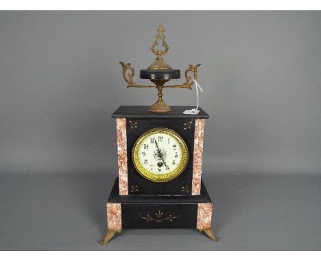 An early 20th century French black and pink marble mantel clock surmounted by a black marble and cast, gilded finial, raised 