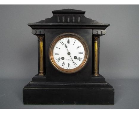 A late 19th century French black slate mantel clock of architectural form, flanked by reeded brass columns with Corinthian ca