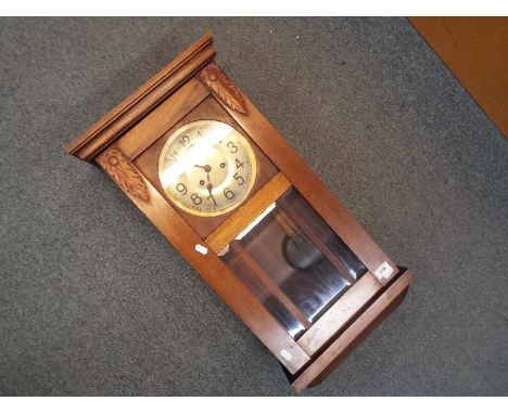 A wood cased, bevelled glazed wall clock, Arabic numerals to the dial, with key and pendulum, approximately 72 cm (h).