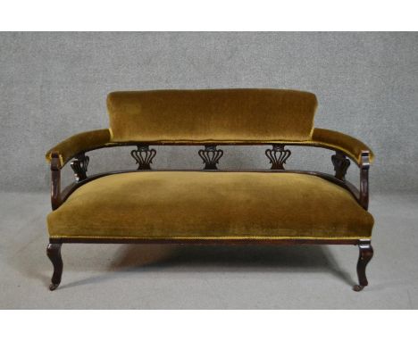 A late Victorian walnut two seater sofa, upholstered to the back and seat in golden velour, with pierced back splats, on cabr