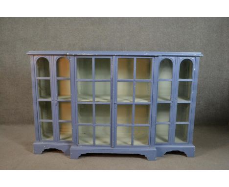 A grey painted wood breakfront display cabinet, with four glazed doors enclosing shelves, on bracket feet. H.103 W.160 D.33cm