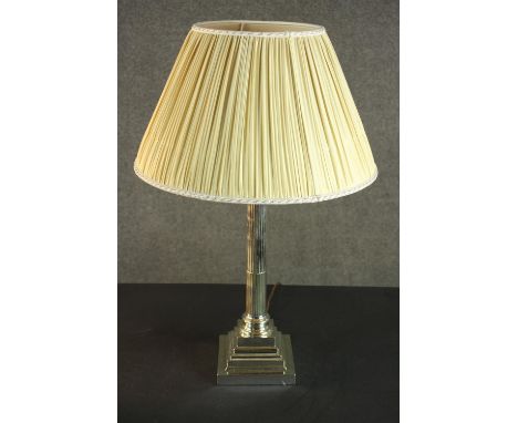 A silver plated Corinthian column candlestick, converted to a table lamp, with a square step-down base and a pleated shade. H