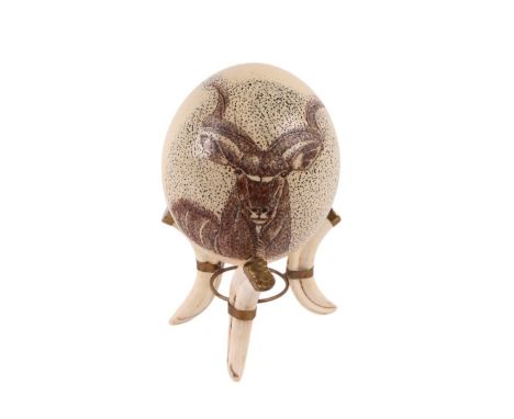 Taxidermy.  An ostrich egg engraved with a kudu on a tripod boar's tusk stand, 20cms high.