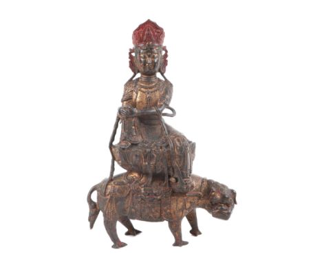 A Chinese gilt bronze group depicting a deity seated on a lotus flower riding the back of a lion, 33cms high.