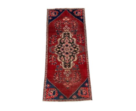 A Persian Baluch runner with central floral medallion and blue spandrels, on a red ground, 95 by 220cms.
