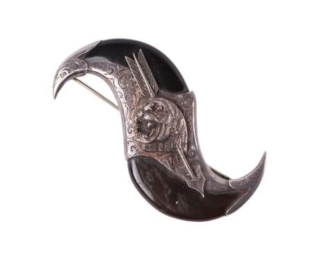 An Indian silver coloured metal and horn brooch in the form of a pair of claws with a tiger mask shot by an arrow, 8.5cms wid