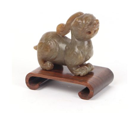 A Chinese jade / hardstone lion dog on a hardwood stand, 5cms long.