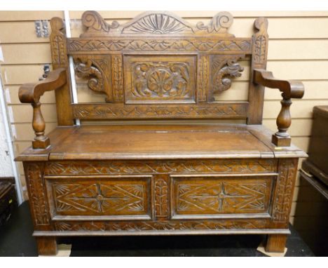 A VINTAGE CARVED OAK BOX SEAT HALL BENCH, the back with carved dragon's heads and floral panels, shaped arms with baluster tu