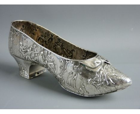 A CONTINENTAL SILVER MODEL OF A PERIOD STYLE SHOE with applied front bow and repousse style repeated decoration of figures wi