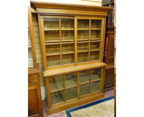A CIRCA 1900 OAK BOOKCASE, the top section with inverted step cornice over twin glazed four panel sliding doors and interior 