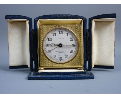 A CIRCA 1920's ZENITH TRAVEL ALARM CLOCK in blue leather fitted case, the dial set with Arabic numerals and John Byrne & Son 