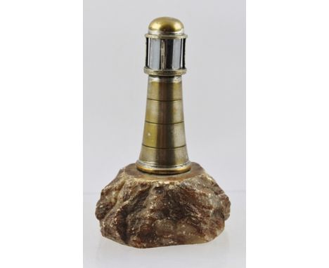 AN EARLY 20TH CENTURY TABLE LIGHTER in the form of a lighthouse, with hinged cover on rock base, 13.5cm high 
