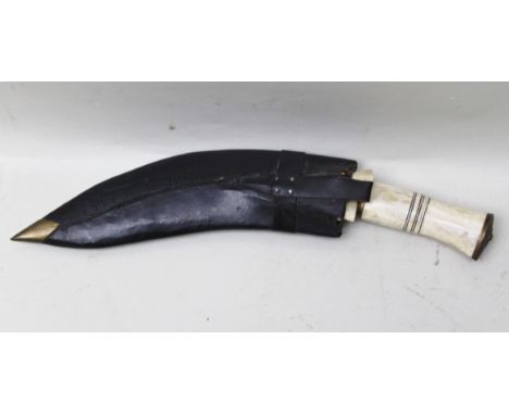 A KUKRI KNIFE with bone handle and brass mounts, in leather scabbard with two small knives inset 