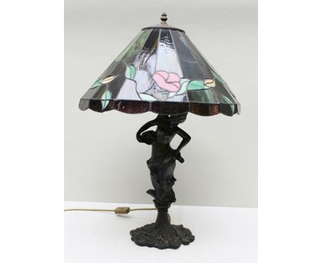 A TIFFANY STYLE TABLE LAMP the bronzed effect cast stem in the form of a lady on water lily base, fitted stained glass shade,