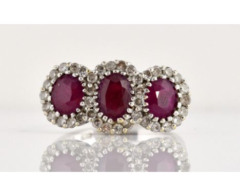 Ruby and diamond triple cluster ring, three oval cut rubies surrounded by round brilliant cut diamonds, mounted in white meta