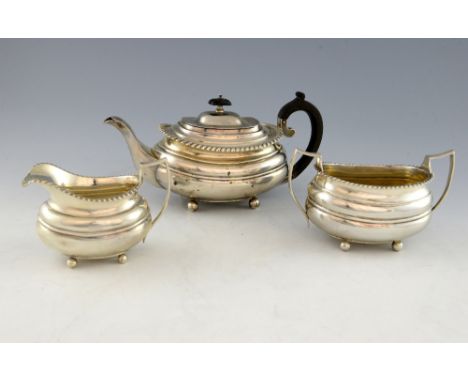 George V silver three piece tea service, comprising tea pot, cream jug and sugar bowl, with gadrooned borders, on four ball f