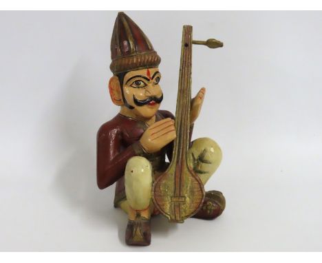 A 20thC. folk art carved wood & hand painted Asian gentleman seated playing a sitar, 305mm tall