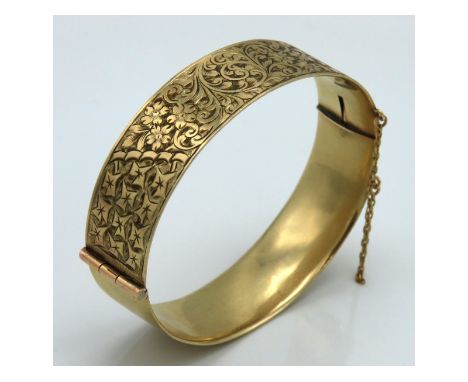 A 9ct gold solid metal core bangle with chased floral decor, 44.6g inclusive, 60mm x 51mm