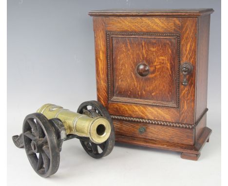 A 1920's oak smokers box, with door and drawer, 33.5cm high, with a brass and cast iron model cannon, 34cm (2)