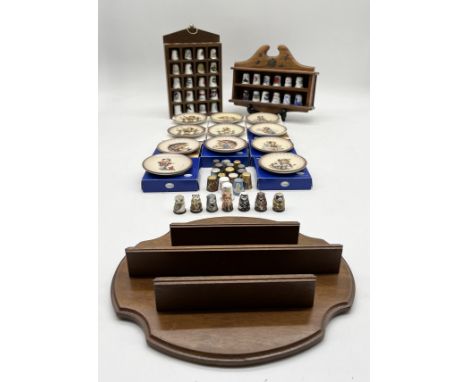 An assortment of M I Hummel miniature plates along with a collection of thimbles and display stands.