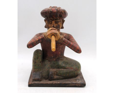 An Eastern painted wooden figure of a seated man playing a pipe - height 26cm