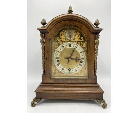 An early 20th century oak mantle clock, the case having gilt metal acorn finial, side mounts and scroll feet, the arched top 