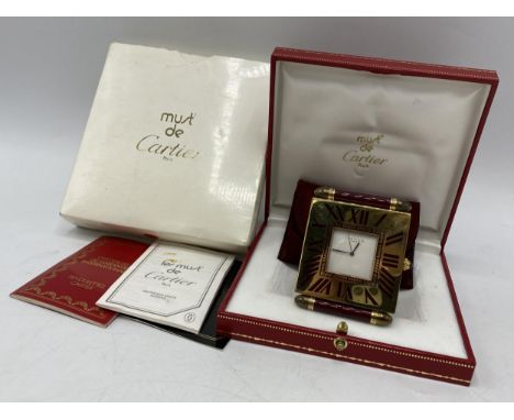 A Cartier quartz folding bedside/travel alarm clock having a white dial in a brass case with burgundy coloured enamel on the 