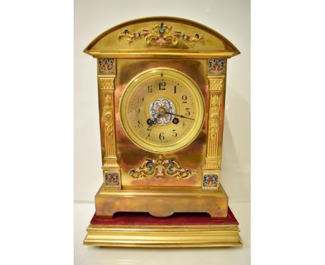 An early 20th century brass mantle clock on a gilded treen stand, the arched top case with floral cloisonné decoration, two p