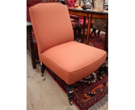 A VICTORIAN LOW OVERSTUFFED UPHOLSTERED CHAIR with square back and seat and standing on ring turned tapering ebonised legs, t