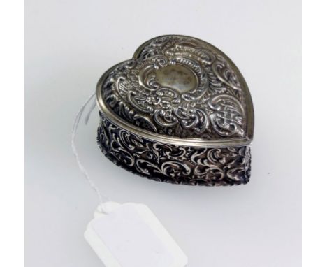 A late Victorian silver heart shaped trinket box, profusely chased and engraved with scrolling foliage around a central vacan