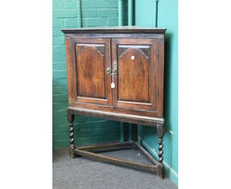 A mid 18th century oak corner cupboard, having a pair of fielded panel doors enclosing a shaped shelf, on a later barley twis