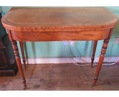 A Georgian mahogany fold-over card table on ring turned supports, terminating on brass castors.