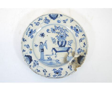 An 18th century English Delft blue and white plate, in the Kangxi style, painted with Chinese figure and table of flowers, wi