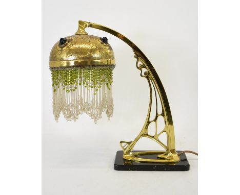 A Secessionist brass table lamp, circa 1900, the open cast arched cantilever support with a textured brass and jewelled shade