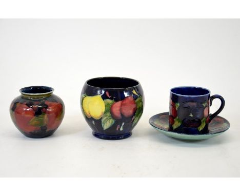 A group of three Moorcroft pieces including a wisteria vase, a pomegranate vase and a pansy can and saucer all on blue ground