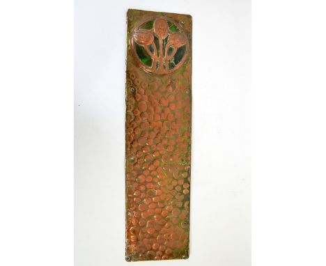 An Arts and Crafts copper door plate, set with a green ceramic cabochon, overlaid with stylised flowers, 58cm long, 15.5cm wi