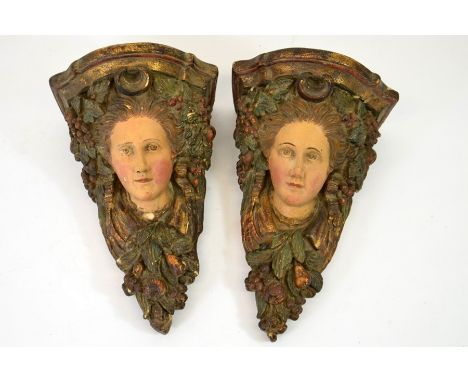 A pair of 19th century wall brackets, painted plaster, modelled in relief as heads and fruit below a shelf, 27cm, long, 16cm 