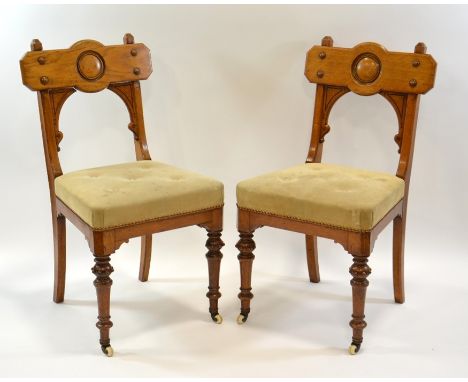 A pair of Gothic Revival oak chairs, circa 1860, the backs with convex roundel and moulded screw caps, below incised brackets