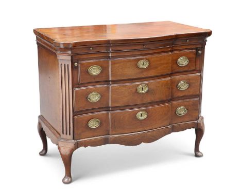 A MAHOGANY COMMODE the shaped molded top above three slides over three long graduated drawers, each fitted with brass oval ba
